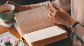 Seseorang sedang menuangkan pikiran ke dalam buku harian di sudut ruangan yang tenang, menciptakan ruang hening untuk merawat kesehatan jiwa di tengah kesibukan harian.