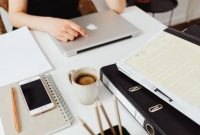 Seseorang sedang mengatur jadwal harian menggunakan buku catatan dan laptop di meja kerja yang tertata rapi untuk menciptakan alur kerja yang efisien.