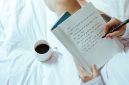 Seorang wanita menikmati momen tenang sembari menulis catatan harian di atas buku agenda kayu dengan secangkir kopi hangat di sampingnya. Kebiasaan menulis ini membantu menenangkan pikiran dan meredakan stres harian secara efektif.