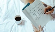 Seorang wanita menikmati momen tenang sembari menulis catatan harian di atas buku agenda kayu dengan secangkir kopi hangat di sampingnya. Kebiasaan menulis ini membantu menenangkan pikiran dan meredakan stres harian secara efektif.