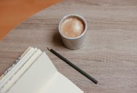 Seseorang sedang menikmati momen refleksi diri dengan menulis buku harian di atas meja kayu hangat, didampingi secangkir kopi untuk menenangkan pikiran.