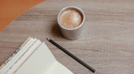 Seseorang sedang menikmati momen refleksi diri dengan menulis buku harian di atas meja kayu hangat, didampingi secangkir kopi untuk menenangkan pikiran.
